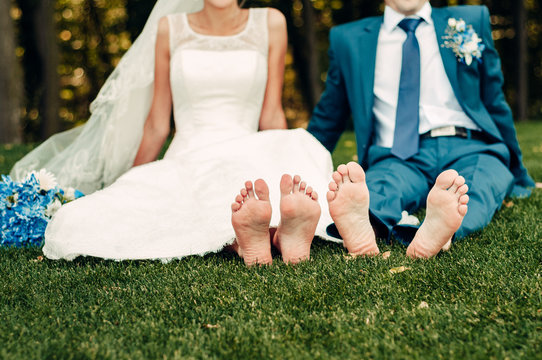 barefooted young fair-haired bride and her fiance sits on the grass in an exotic park, in a long white dress with a bouquet of flowers in her hands, a walk after the wedding ceremony