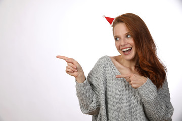 Hübsche rothaarige Frau mit kleiner Weihnachtsmütze lacht und zeigt in eine Richtung