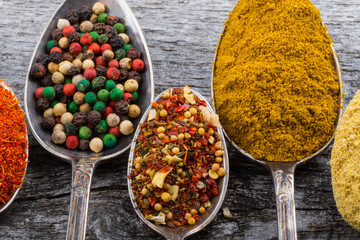Antic metal spoons with different kinds of spices on old wooden board. Selective focus