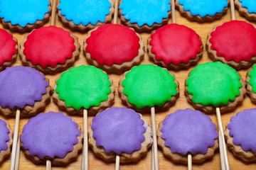 Gingerbread cookies with colored mastic on sticks on the old wooden cutting board