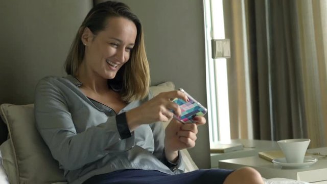 Young businesswoman playing game on smartphone lying on bed at home 
