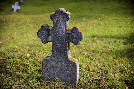 Old, stone, tombstone cross on a background of green grass.