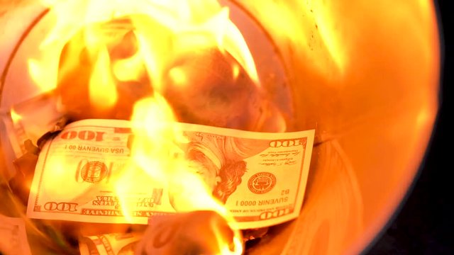 Burning dollars in the trash can close-up and a man throws new bills into the fire. Slow motion
