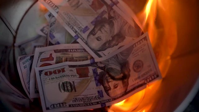 Burning dollars in the trash can close-up and a man throws new bills into the fire. Slow motion