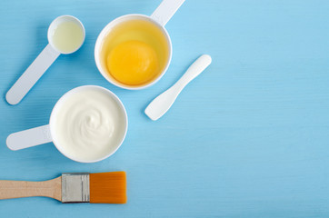 Sour cream (greek yogurt), raw egg and olive oil in a small plastic scoops - ingredients for preparing diy masks, scrubs and moisturizers. Homemade cosmetics. Top view, copy space