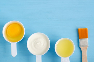 Sour cream (greek yogurt), raw egg and olive oil in a small plastic scoops - ingredients for preparing diy masks, scrubs and moisturizers. Homemade cosmetics. Top view, copy space.