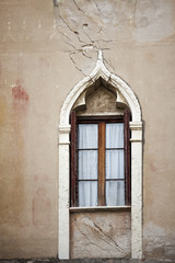 Fototapeta na wymiar Withered facade with window of an old Italian town house. Cracks in the wall. Byzantine frame.