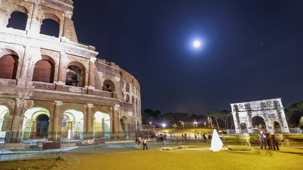 Fototapeta na wymiar Roman Colosseum and Constantine Arch by night with tourists and photographers with a bride for marriage night photo shooting in Rome, Italy.