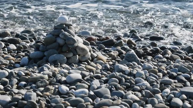 Entertainment for beachgoers. Cairn, cone is formed of pebbles on seashore, with waves always
