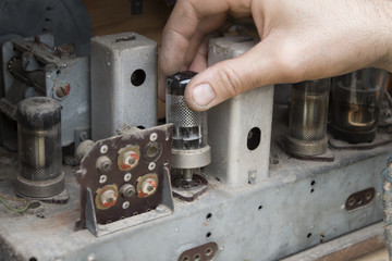 Dłoń mężczyzny wyciąga lampę ze starego zabytkowego lampowego radia.