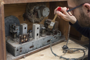 15.	Mężczyzna czyści z kurzu stare lampowe zabytkowe radio za pomocą pędzla. - obrazy, fototapety, plakaty