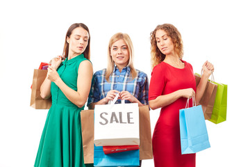 Portrait of three young woman holding bunches of multi-colored shopping bags after sale