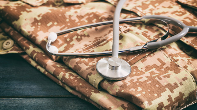 USA army health care. Military digital pattern uniform and medical stethoscope on blue wooden background, closeup view