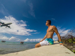 Fototapeta na wymiar Muscular man on the coast watching landing of airplane flying over the sea of caribbean sea. Montego Bay. Jamaica. 2017