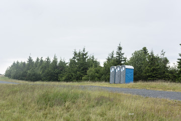 Plastic toilet next to a forest on a meadow in the mountains.