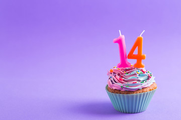Festive creamy cupcake with sprinkles and candles in the form of number 14 on purple background - obrazy, fototapety, plakaty