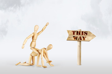 Man rides on another person in the direction of the road sign. Abstract image with wooden puppets