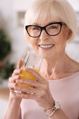 Close up of a cheerful senior woman drinking orange juice