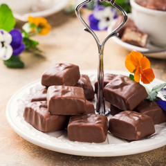 Soft nougat chocolate sweets on white plate with pansy flowers. Party food concept.