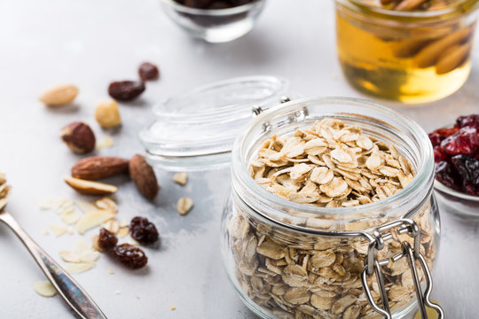 Ingredients for homemade oatmeal granola in glass jar. Oat flakes, honey, raisins and nuts. Healthy breakfast concept with copy space.