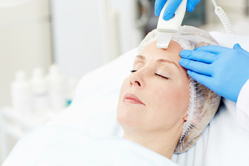 Woman with aging skin having facial care procedure while visiting beautician