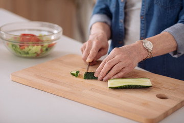Close up of a pleasant senior woman cutting cucumbers