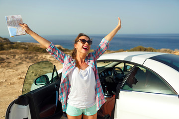 Joyful woman with a map in her hand traveling on a cabriolet