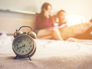 Young lovely couple sitting on bed, using computer for shopping in free time in the morning. Alam clock on edge of the bed.