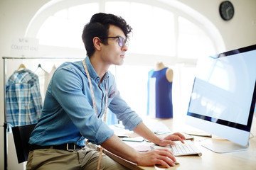 Young creative fashion designer sitting in front of computer and searching in the net for new looks and tendencies