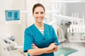 Happy young dentist or surgeon in uniform with crossed arms on her chest