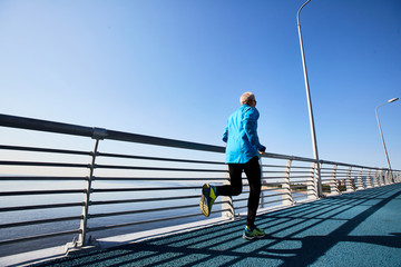 Back view of aged runner training by riverside in the morning