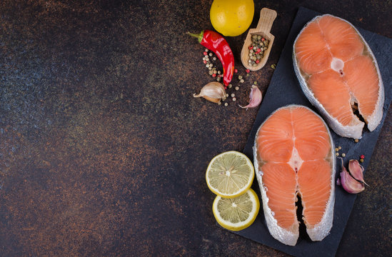 Two fresh raw salmon steaks on slate board with salt, peppers, lemon on dark table background, top view. Healthy Dieting Food Concept