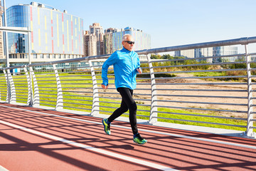 Retired man in activewear jogging along railings with cityscape behind