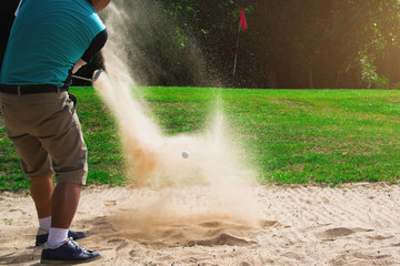 Golfers hit the ball in the sand.
