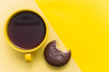 yellow mug with black coffee and a chocolate macaron on a yellow background.