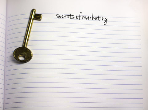 secrets of marketing handwriiten text on a blank white empty paper with a key on the side and copy space
