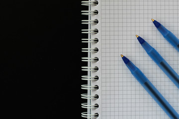 Notepad squared with three blue pens for education, business with copy space top view on black background