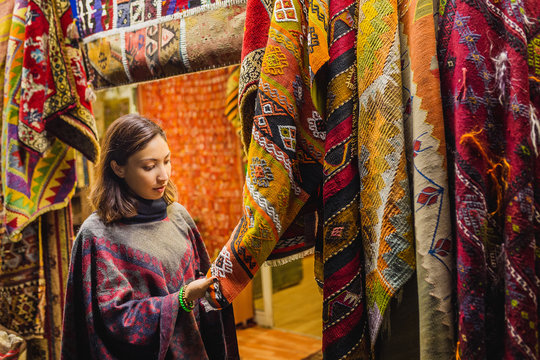 Young Woman Shopping For A New traditional oriental poncho or carpet at tourist market in Cappadocia. Middle east fashion and clothes concept