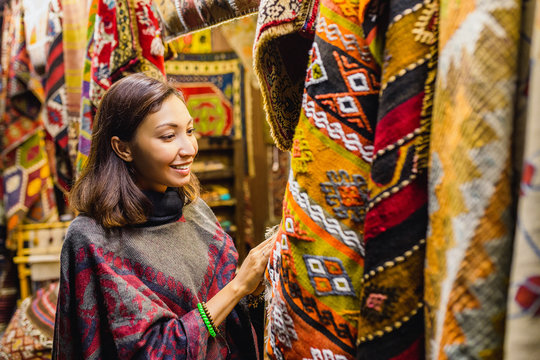 Young Woman Shopping For A New traditional oriental poncho or carpet at tourist market in Cappadocia. Middle east fashion and clothes concept