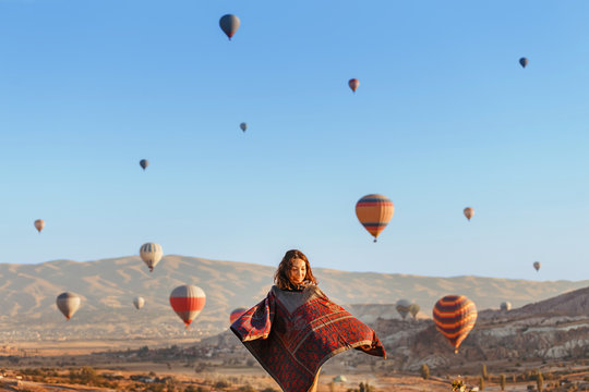 A tourist girl on a mountain top enjoying wonderful view of the sunrise and balloons in Cappadocia. Happy Travel in Turkey concept