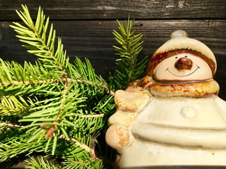 herziger, freundlich lächelnder schneemann aus keramik neben einem grünen fichtenzweig, vor einer...