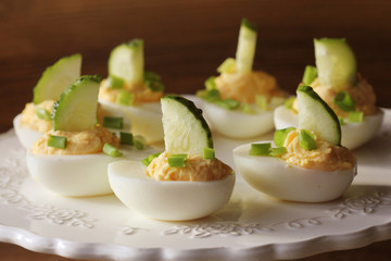 Spicy deviled eggs garnished with cucumber and leek on white plate. Wooden rustic background