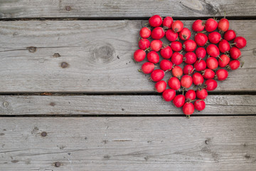 Red heart of hawthorn berries on a wooden background. - obrazy, fototapety, plakaty