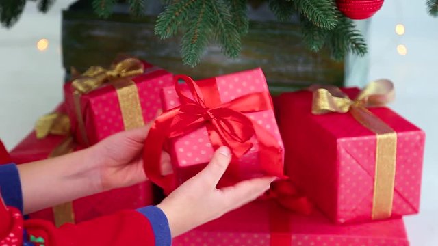 Closeup of small hands of little kid dressed in red night pajamas. White happy child looks at holiday presents near Christmas tree. Real time full hd video footage.