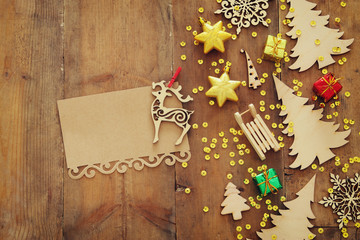 Top view image of christmas festive decorations next to empty note on old wooden background