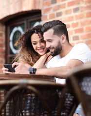 Happy loving  couple using a smartphone sitting in terrace