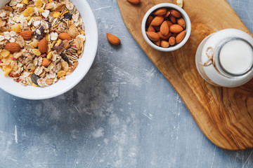 Top view of breakfast with muesli with almond nuts and dried berries in white bowl and the bottle of milk on the blue textured table..