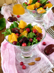 Fruit salad with orange pieces, cranberries, date fruits and arugula in a glass salad bowl