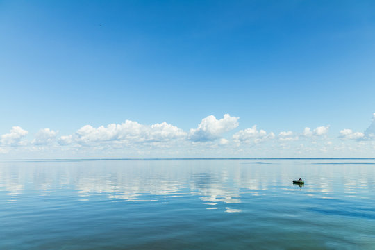 Amazing beautiful blue sky with light white clouds over calm smooth river surface. Summertime. Sunny day.