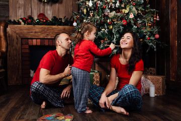 The family in pajamas plays next to a Christmas tree and a fireplace.